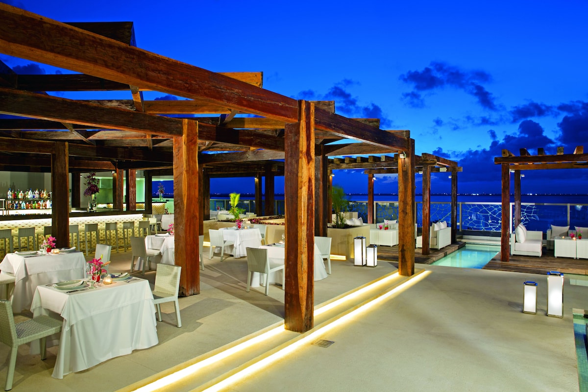 Infinity pool overlooking the Caribbean Sea at Secrets The Vine Cancun, with modern loungers and sunset lighting.