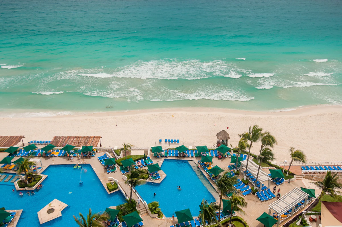 Aerial view of Royal Solaris Cancun’s beachfront pool area, with turquoise waters, palm trees, and sun loungers arranged in a symmetrical layout.