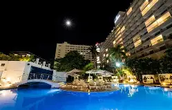 Outdoor pool area at Hotel Emporio Acapulco with ocean backdrop and shaded loungers.